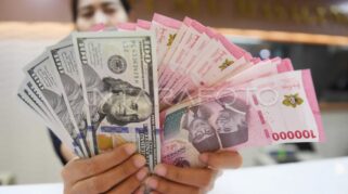 Seorang pedagang valuta asing memamerkan lembaran uang rupiah dan dolar AS. (Foto Istimewa)